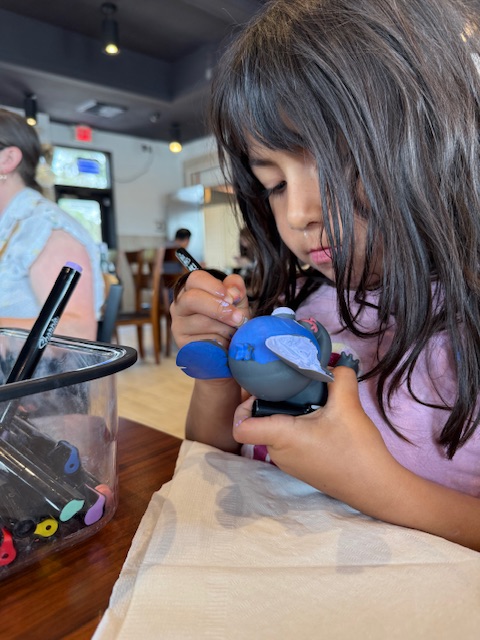Young girl concentrating while carefully painting a blue Stitch Paint Pal with a small brush